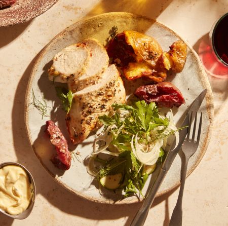 A plate with a prepared meal of roasted chicken with crispy smashed potatoes and a salad of fennel, arugula, and herbs.